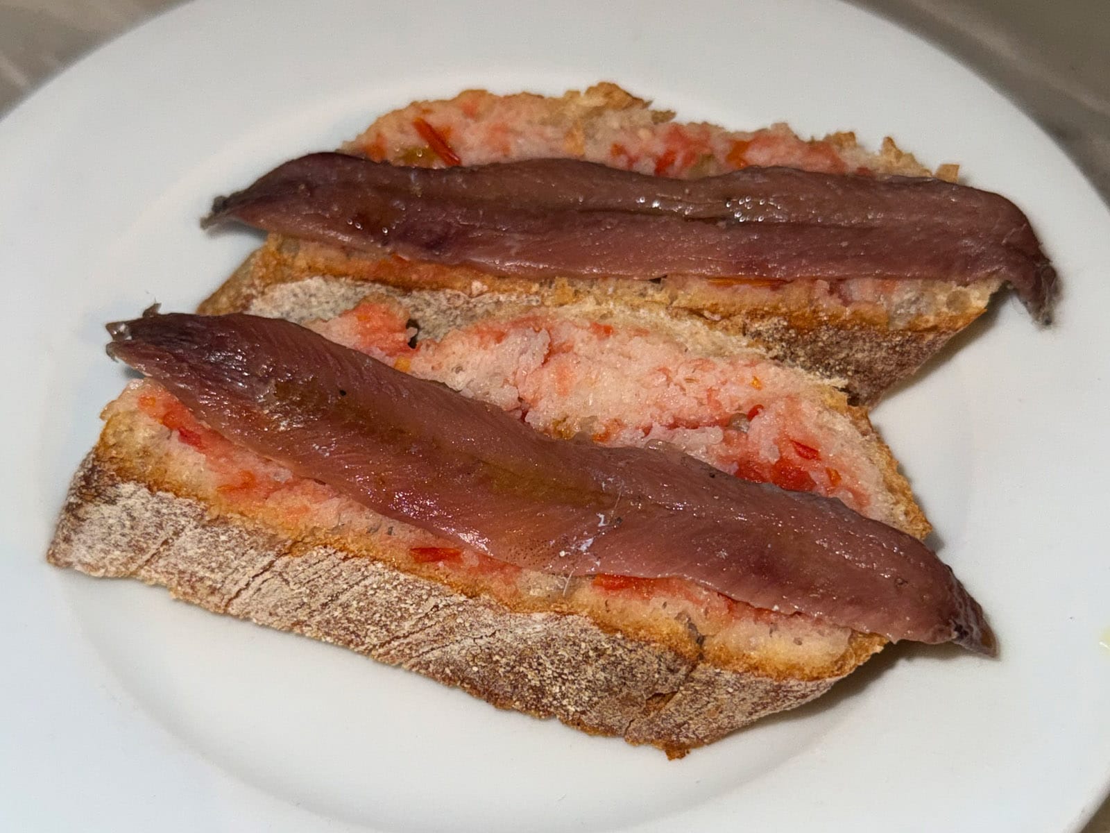 Dos pinchos de anchoa del Bar La Plata: lomos de anchoa sobre rebanadas de pan con tomate, en plato blanco