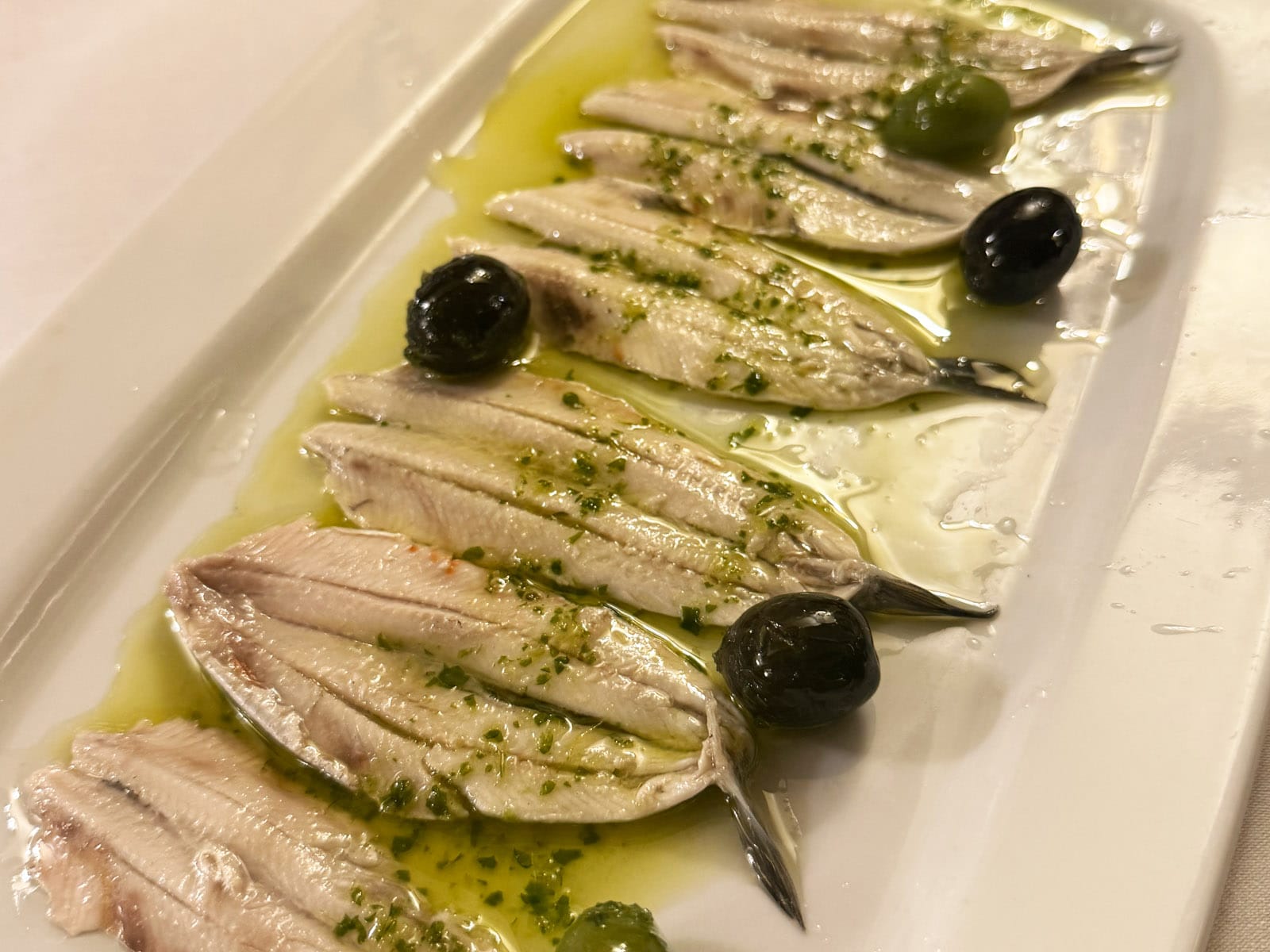 Boquerones en vinagre de Can Culleretes: lomos blancos alineados en fuente alargada, con aceite de oliva, perejil picado y aceitunas