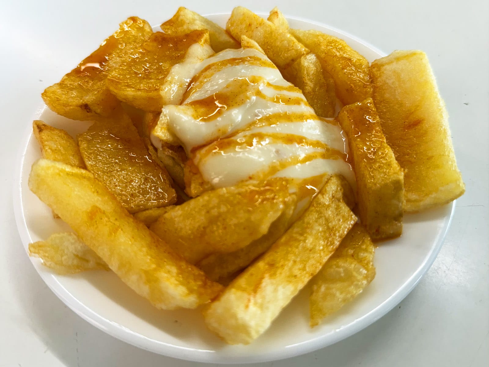 Ración de patatas bravas del Bar Tomás de Sarrià: patata cortada gruesa e irregular, allioli blanco por encima y el aceite picante de receta secreta