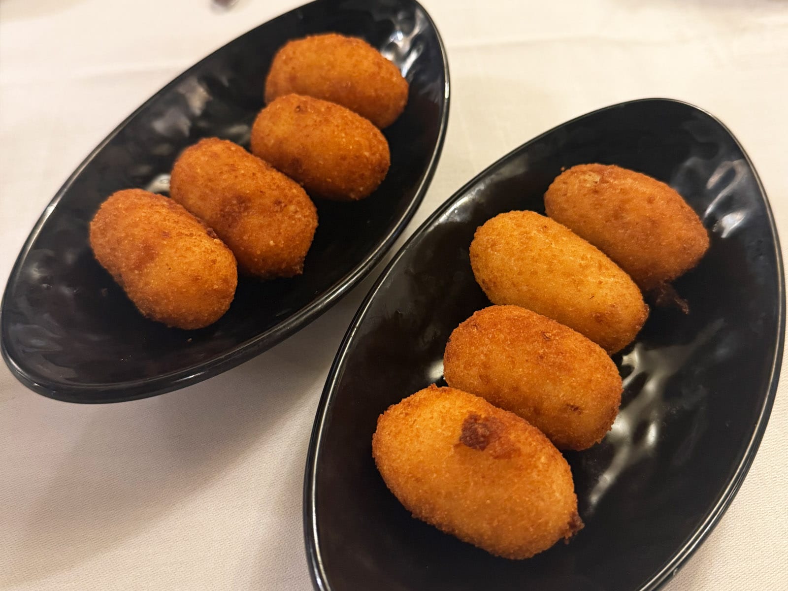 Croquetas de Can Culleretes: ocho piezas doradas servidas en dos platos ovalados negros