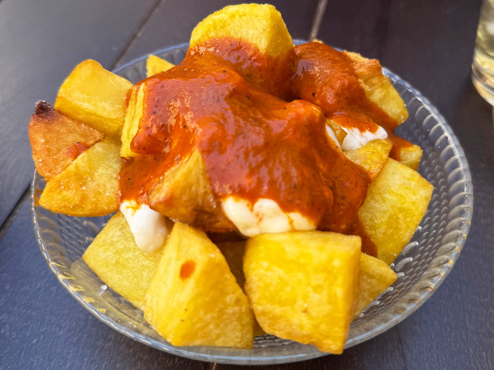 Patatas bravas cortadas en trozos grandes con salsa rojiza y salsa blanca en un plato de cristal