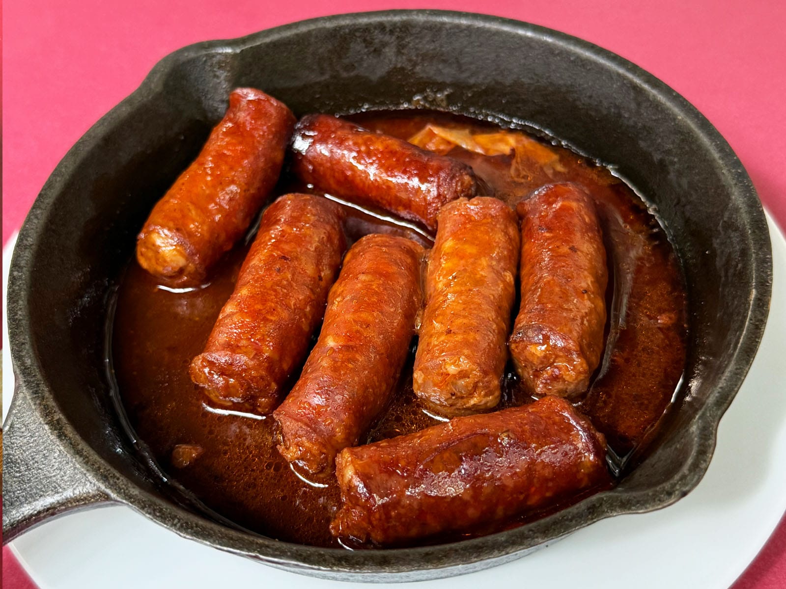 Chistorra al txakoli del Canut: siete trozos de chistorra en una cazuela de hierro con su salsa reducida de color rojo intenso