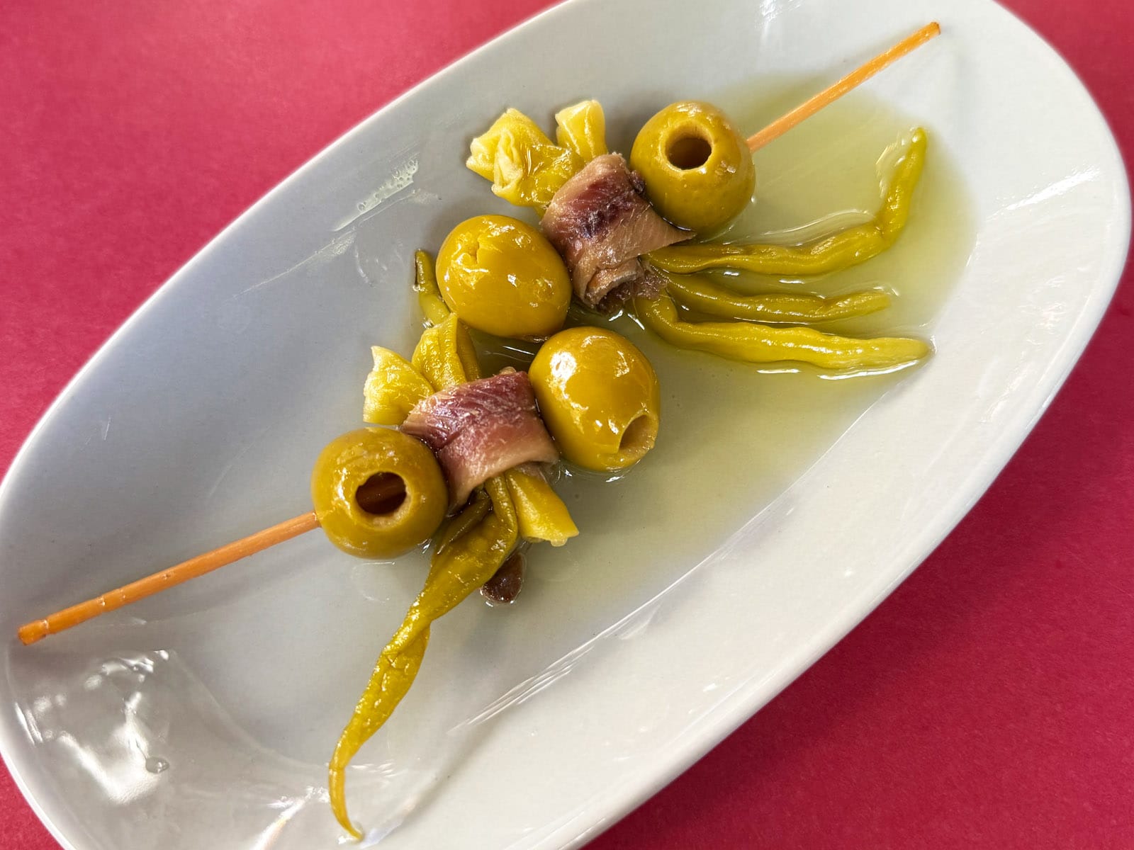 Dos gildas del Canut en fuente blanca: aceituna, guindilla y anchoa ensartadas en palillo, con guindillas y aceite alrededor