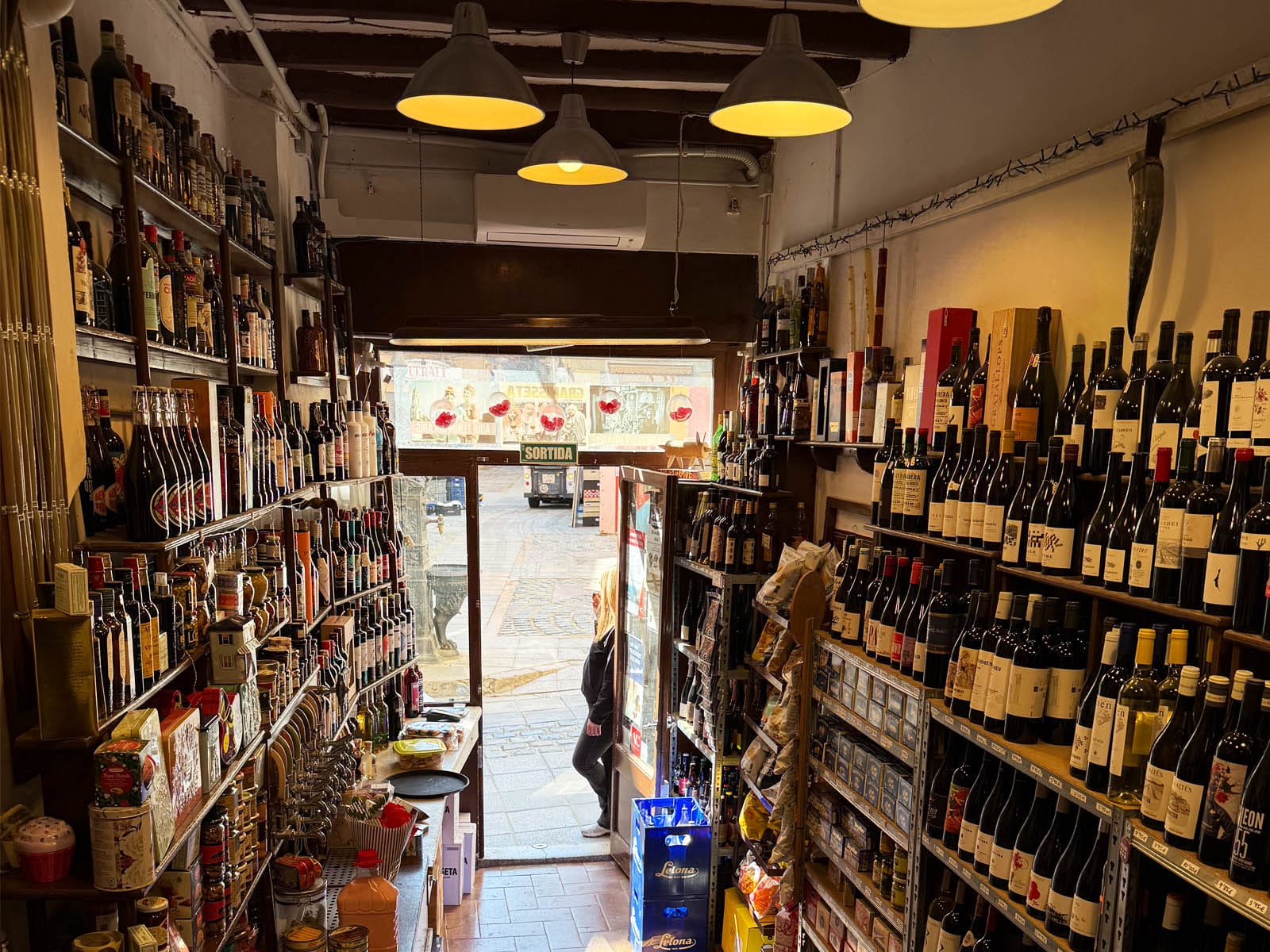 Interior de Magatzem del Vermut con estanterías de botellas a ambos lados y lámparas colgantes